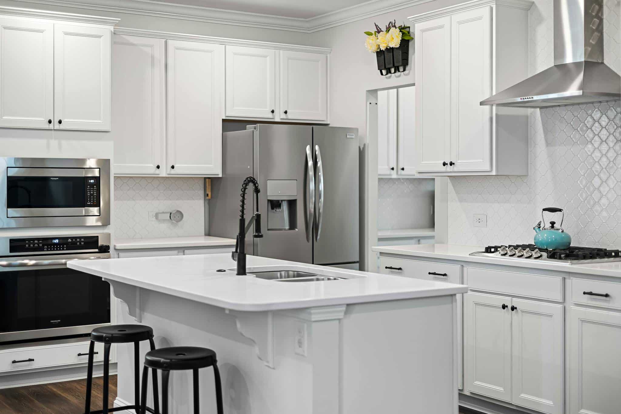 Spacious and elegant white kitchen with modern appliances, island, and stylish decor.